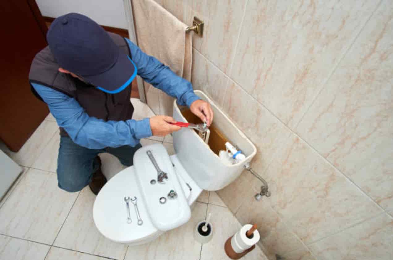 Plumber repairing toilet in residential bathroom