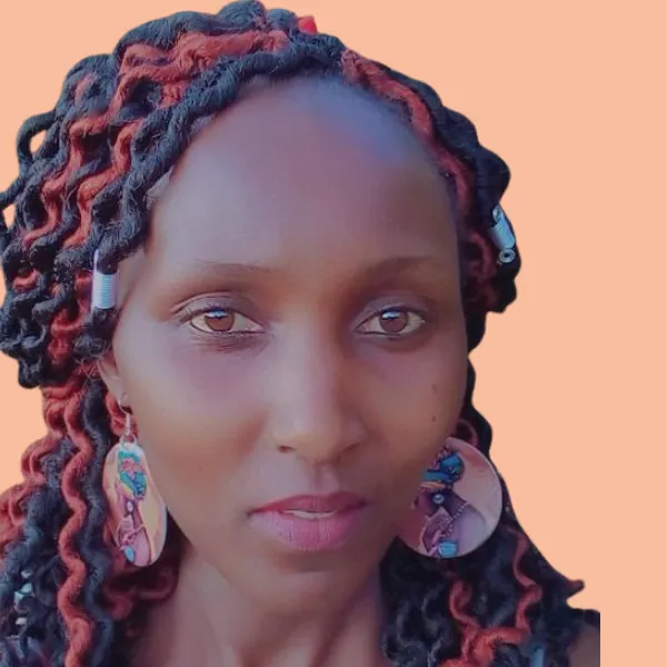 Catherine, a Black Kenyan woman with curly red and black hair and oversized circular earrings, looks directly to the camera. 