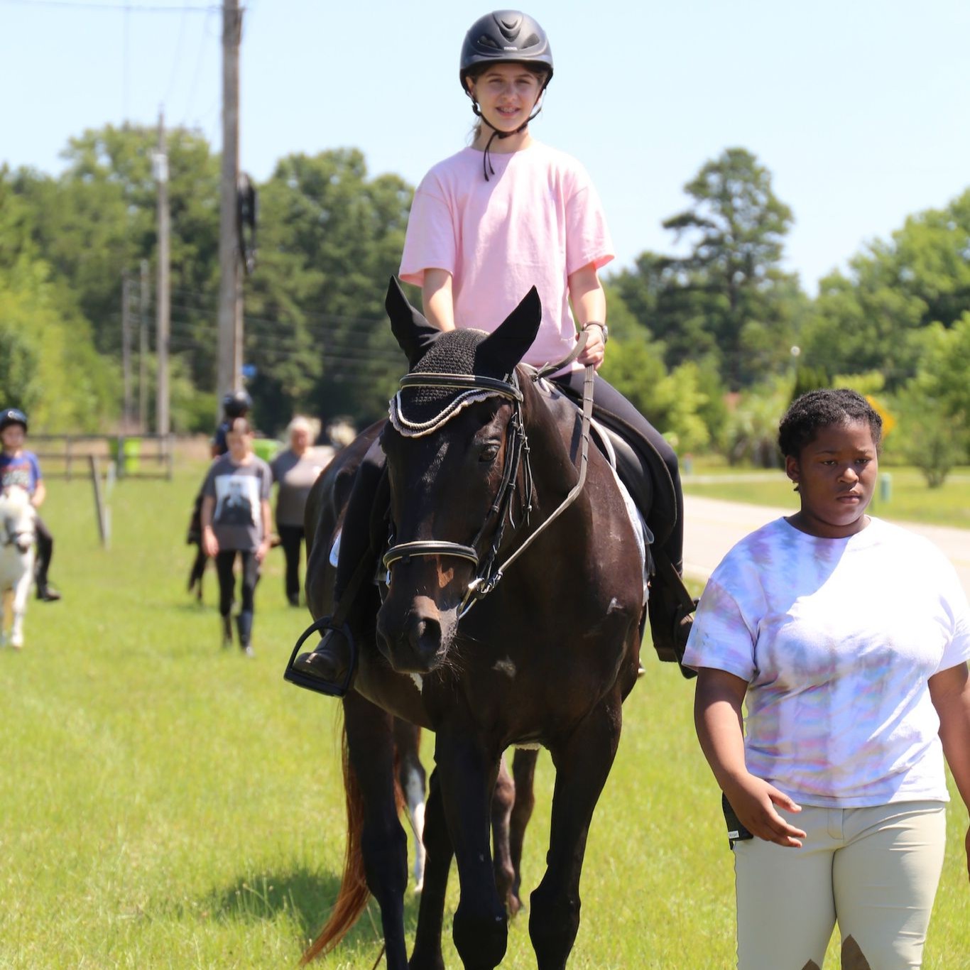 Child riding a dark horse with instructor walking beside during Spring Break Horse Camp in Hopkins SC