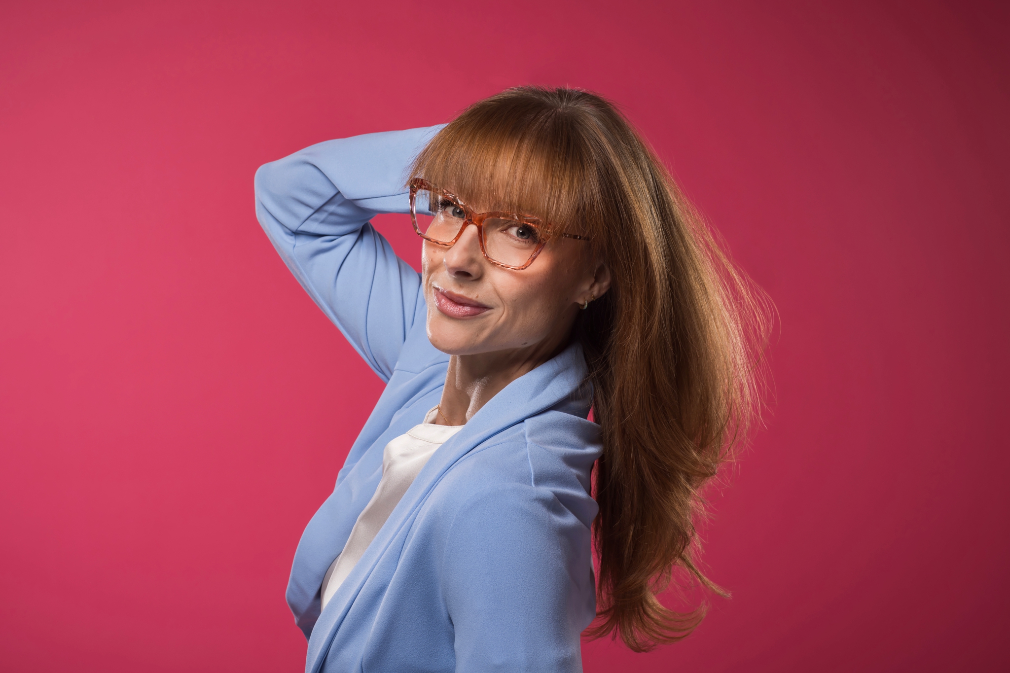 A 40+ woman looking thoughtfully in a mirror with warm lighting, reflecting on her hair's natural evolution.