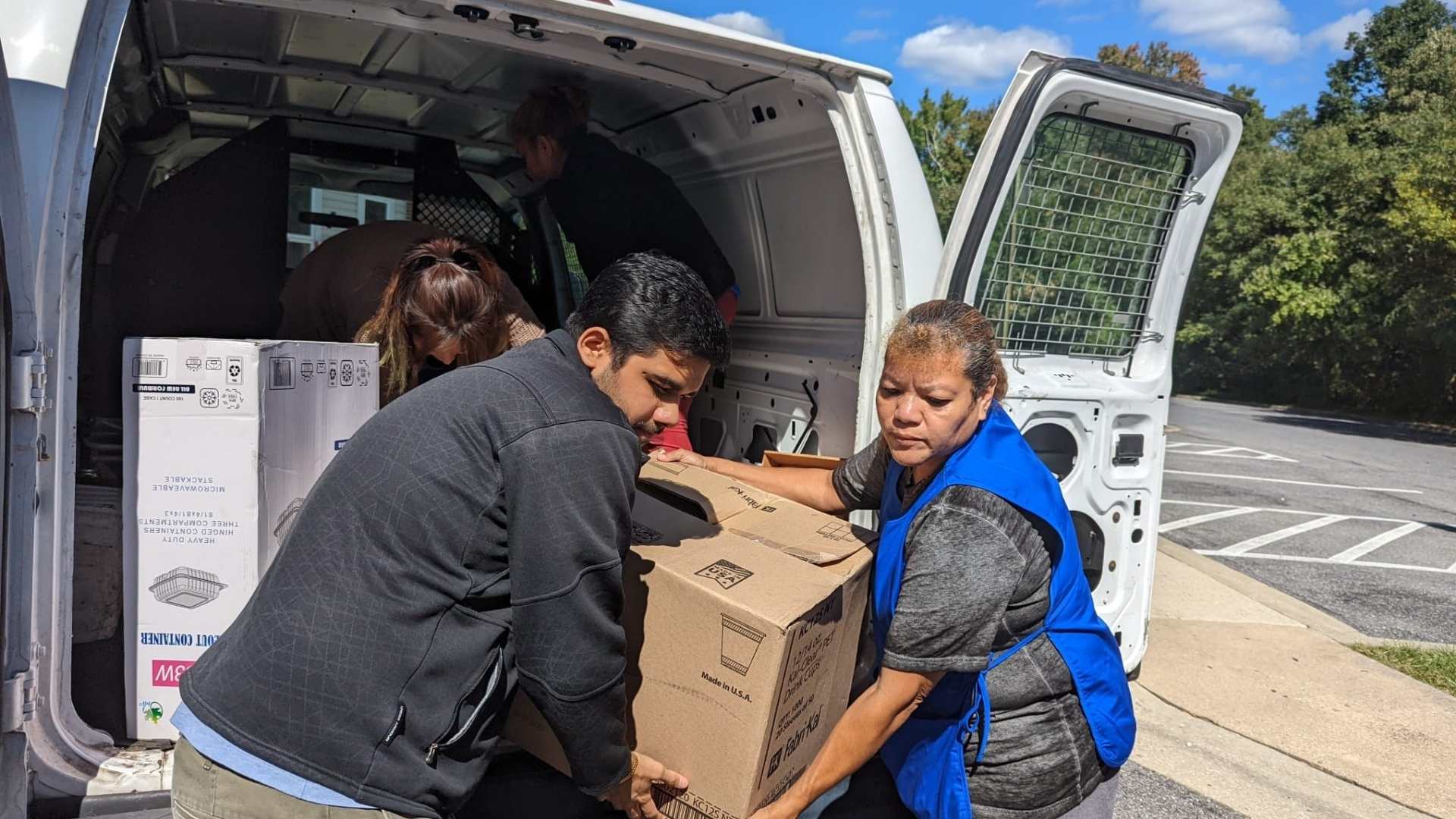 A Crystal Maids cleaning professional in a blue uniform carrying a professional vacuum and a caddy full of cleaning supplies.