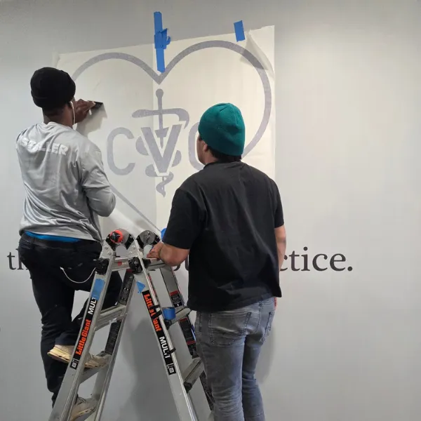 Professional sign installers applying a custom vinyl wall mural for a veterinary practice, showcasing the Signary Custom Signs team at work.