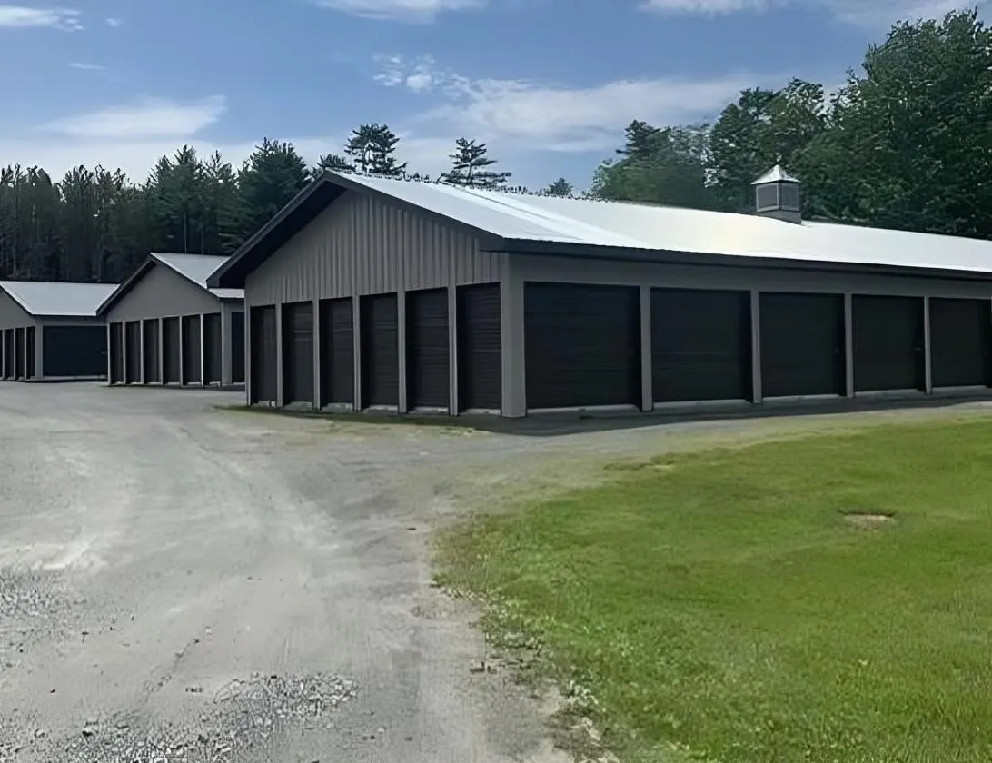 Angled view of multiple storage units with a gravel driveway and surrounding trees at Olsen's Properties