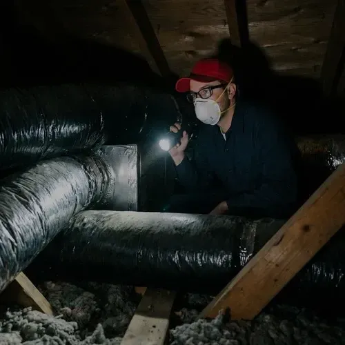 Technician inspecting flexible insulated ducts during a residential ductwork repair service in an attic.