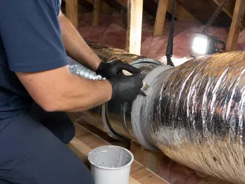 HVAC technician applying duct sealant to a residential duct joint in a Florida attic.