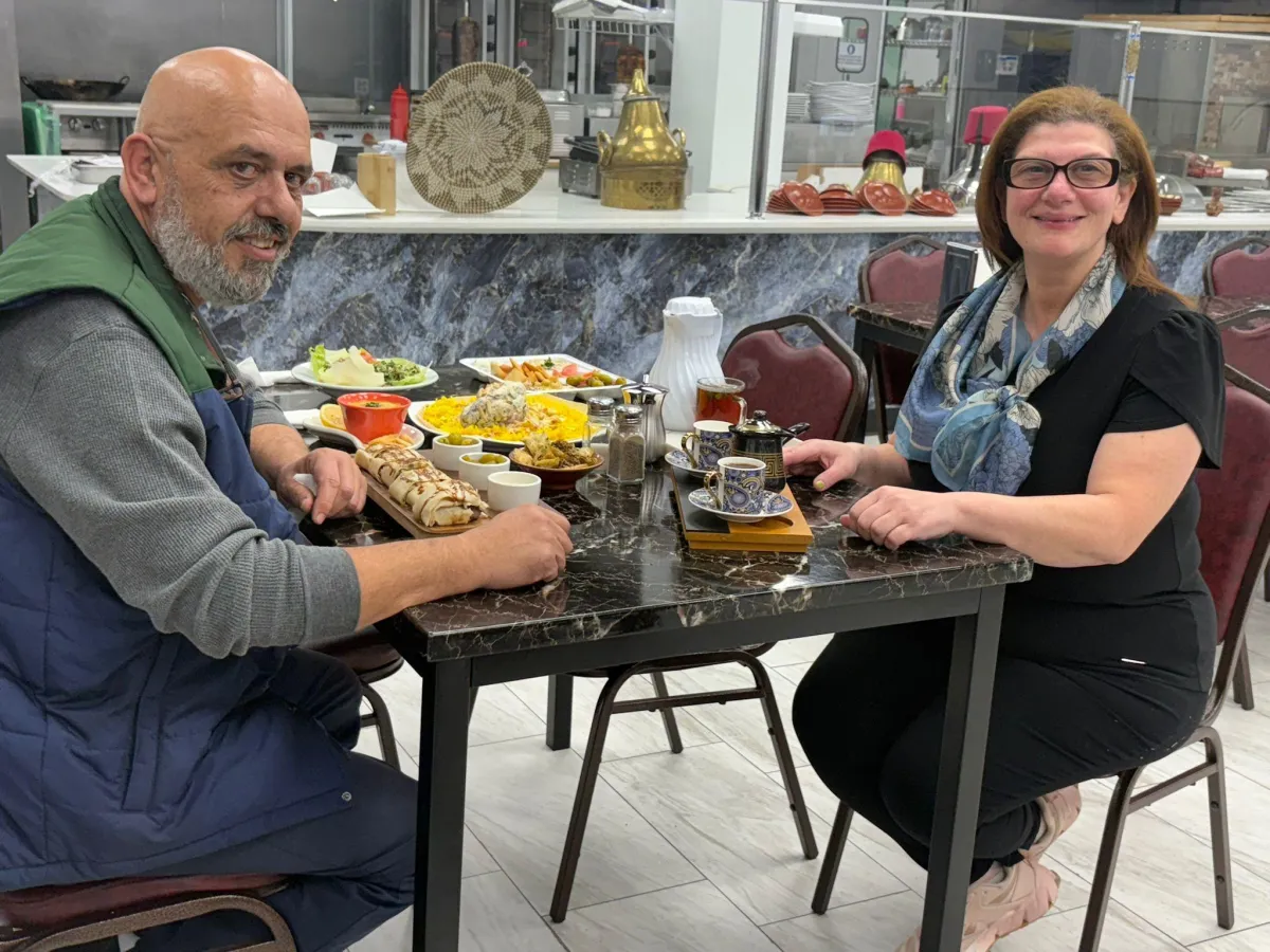 A warmly lit, modern restaurant interior with Mediterranean decor, featuring a welcoming host at the entrance, ready to greet guests, conveying approachability and readiness to serve.