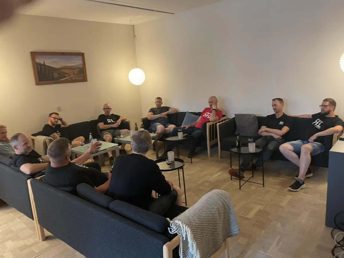 Ti mænd sidder i en sofa og snakker.