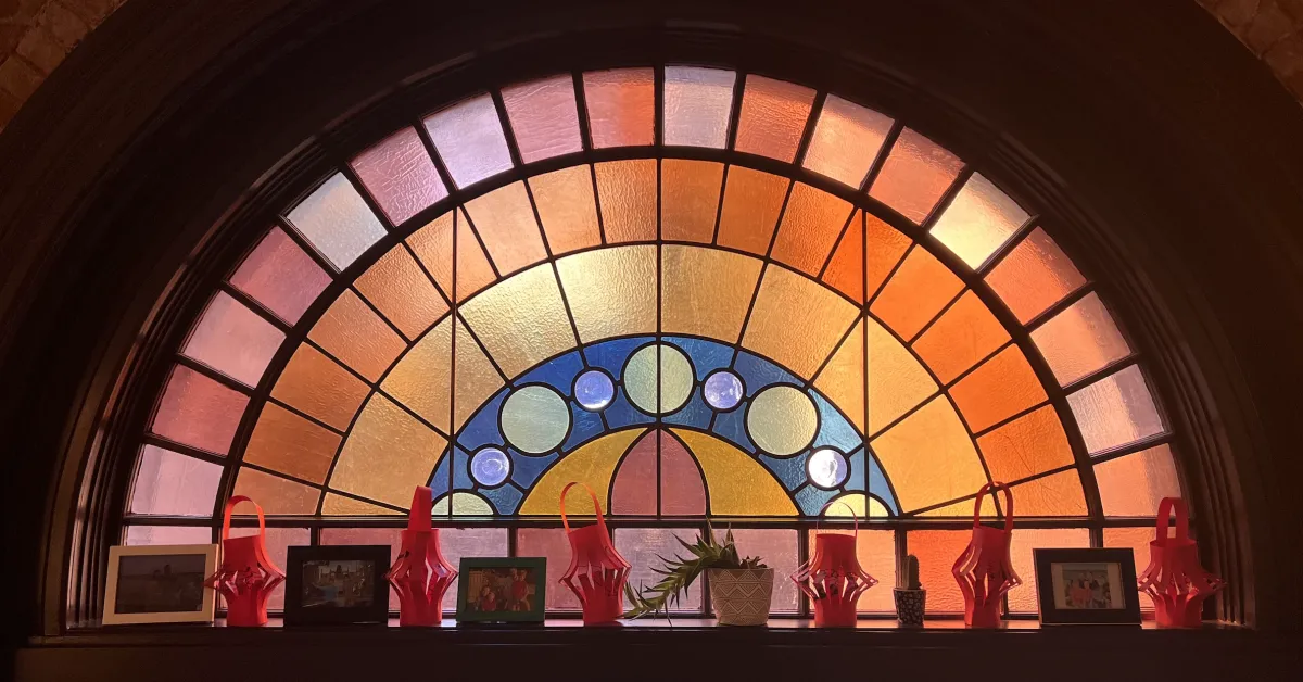 Arched stained-glass window inside Kingsley Montessori School’s building, with warm amber and blue tones and decorative objects arranged on the windowsill.