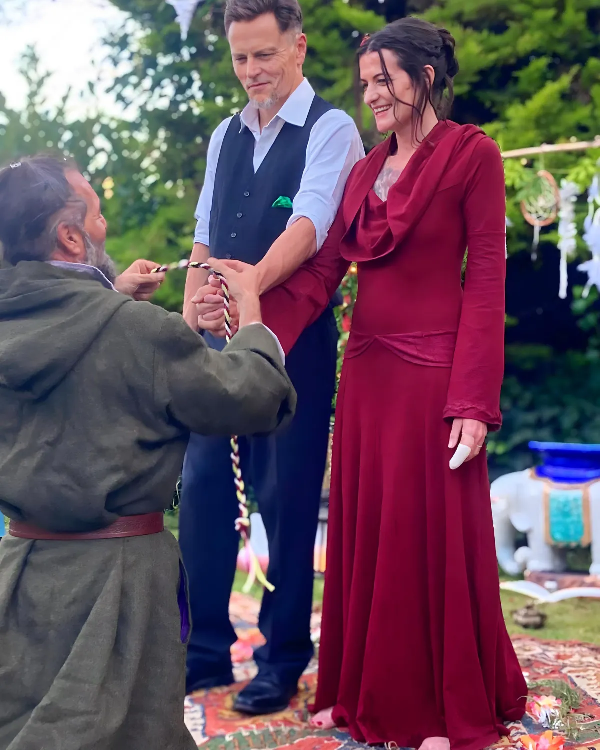 Couple in red and blue attire during a handfasting ceremony, symbolizing sacred union, divine love, and the celebration of spiritual commitment.