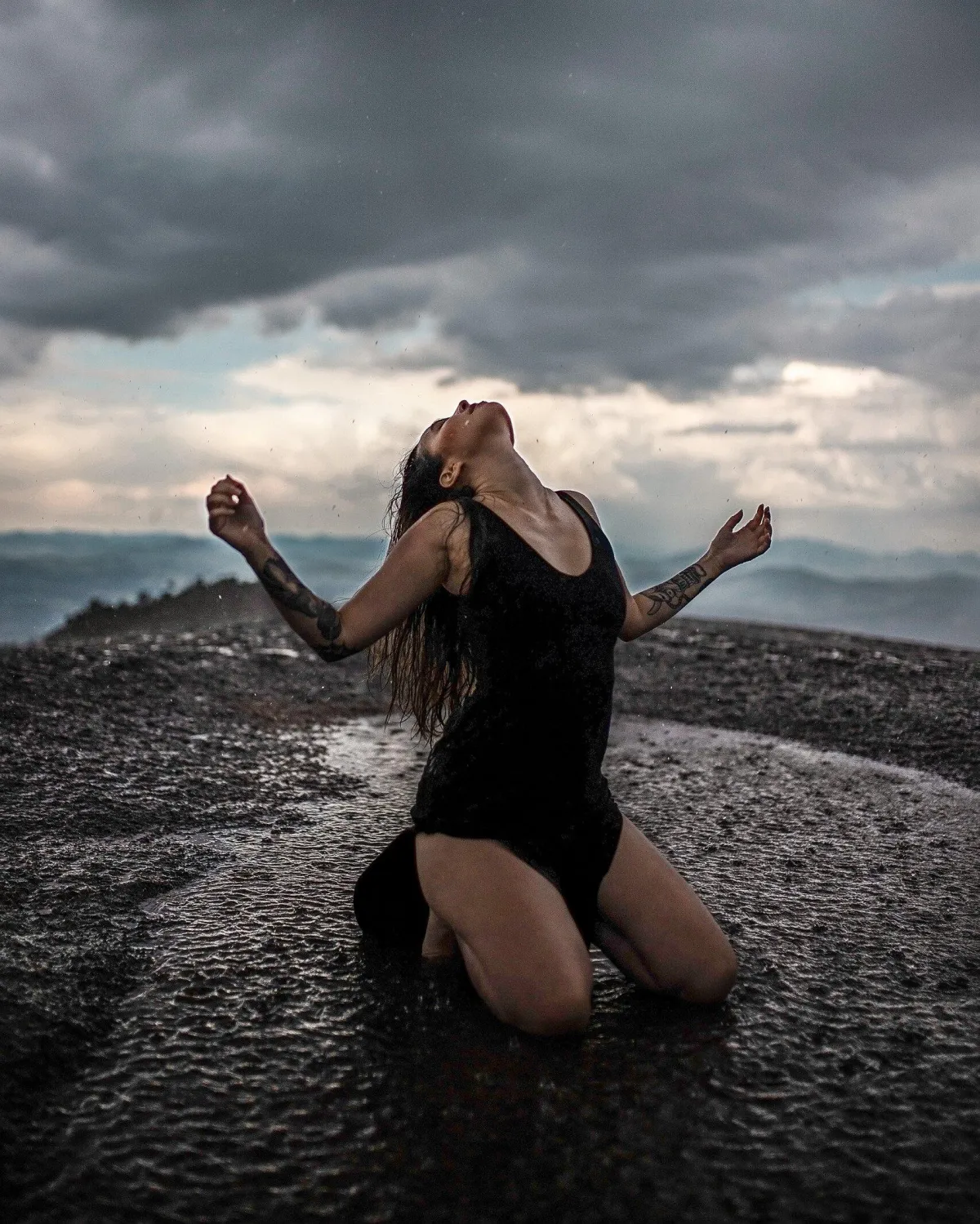 Woman kneeling on a sandy beach near a circle of stones, symbolizing grounding, sacred rituals, and connecting with nature and the divine feminine.