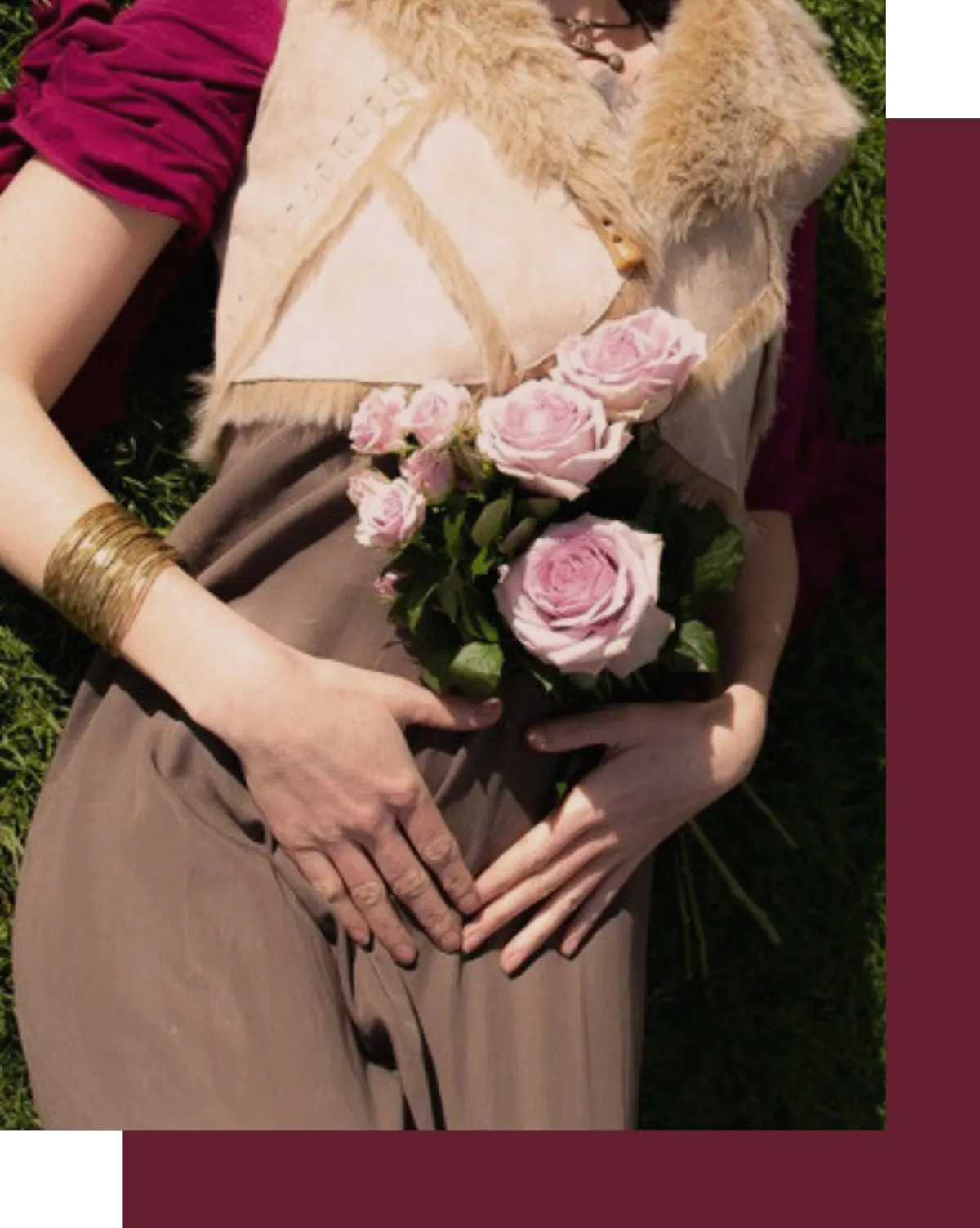 Woman lying on grass, wearing a fur-trimmed vest and earthy-toned dress, holding pink roses over her womb area. Her hands rest gently on her lower abdomen, evoking themes of feminine healing, womb connection, and sacred embodiment. The image captures the essence of deep feminine exploration, rebirth, and the nurturing power of the divine feminine, aligned with themes of womb healing, sacred self-care, and spiritual awakening.