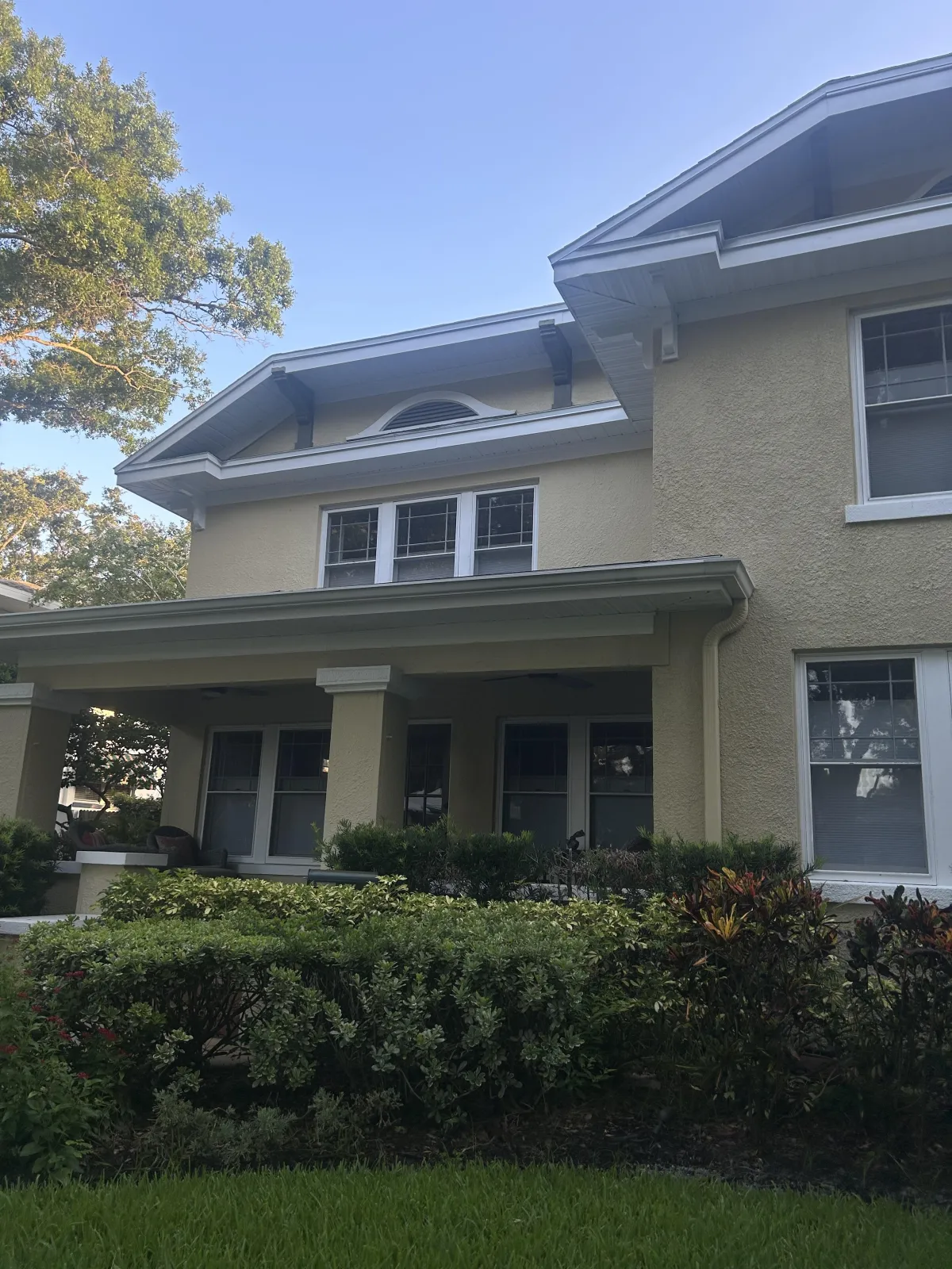 Medium house with tan stucco, 5 windows, and shrubs and grass in front 