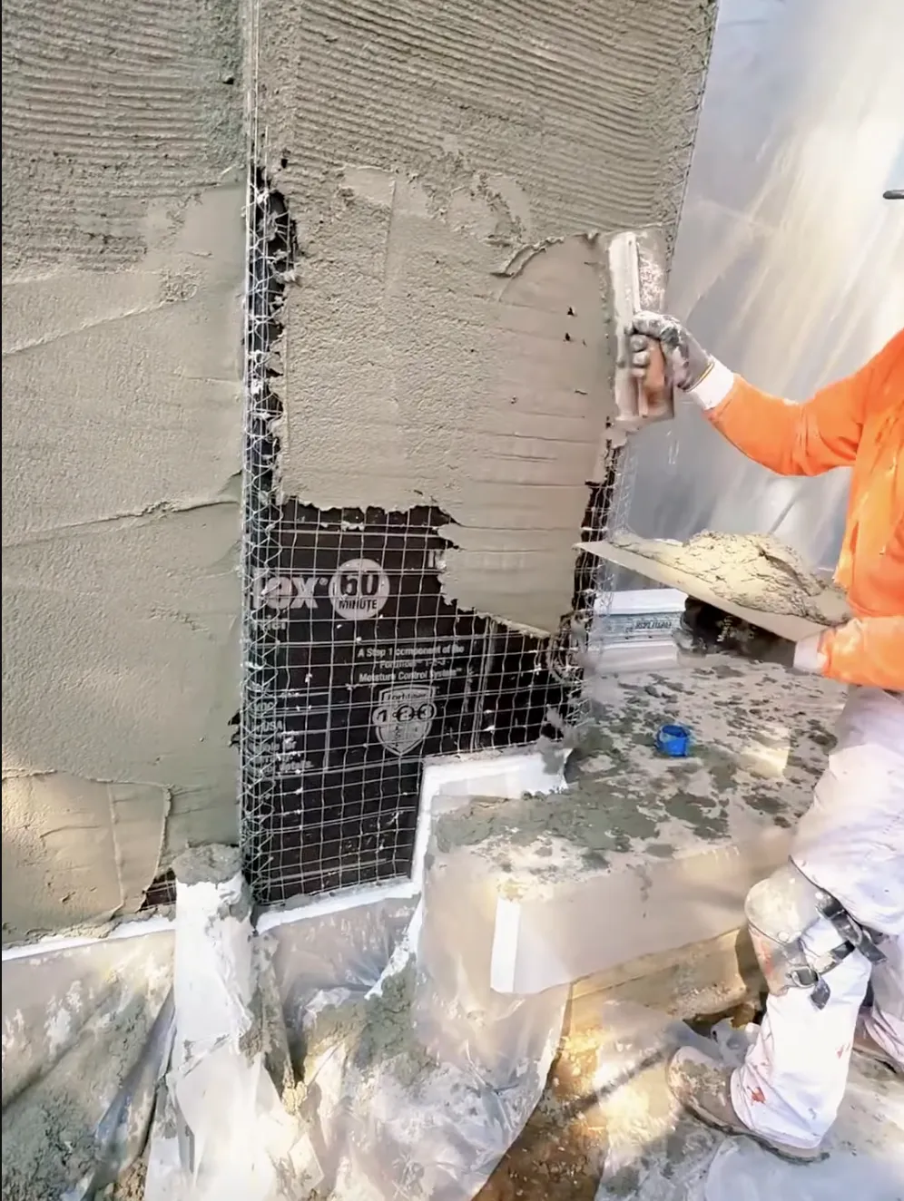 Man with orange shirt applying new stucco to a wall