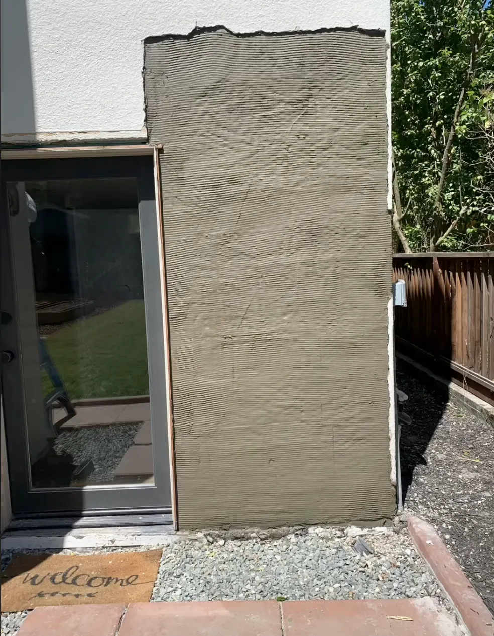 Waterproofing sealing stucco on grey wall with welcome matt in front and door next to it