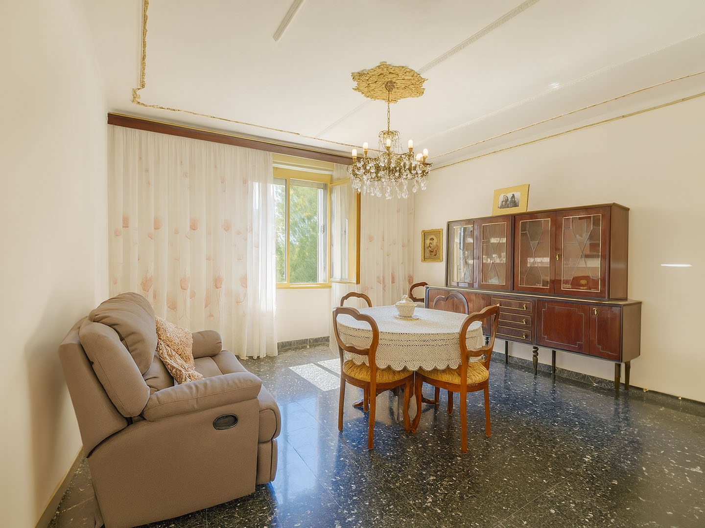 Formal dining area with a sculpted glass table, designer chairs, and a statement chandelier, set against a backdrop of city lights. 3:2 aspect ratio.