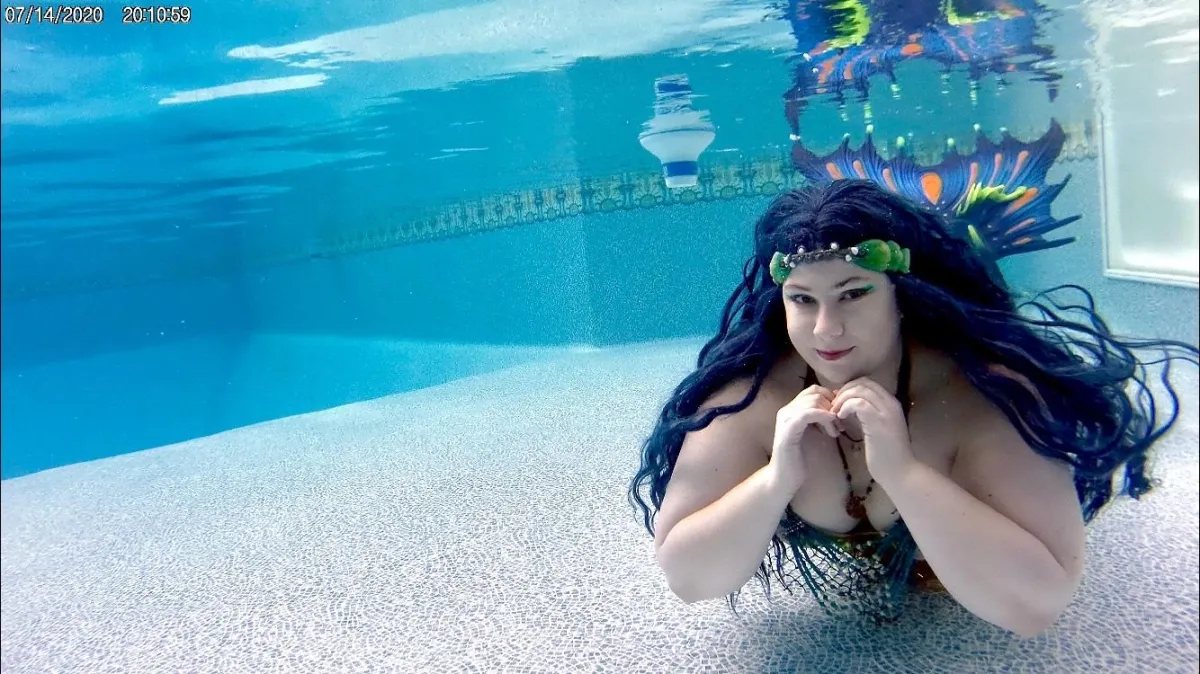 Mermaid Cetea in a pool, fluke visible above head. Hands make a heart shape below her chin