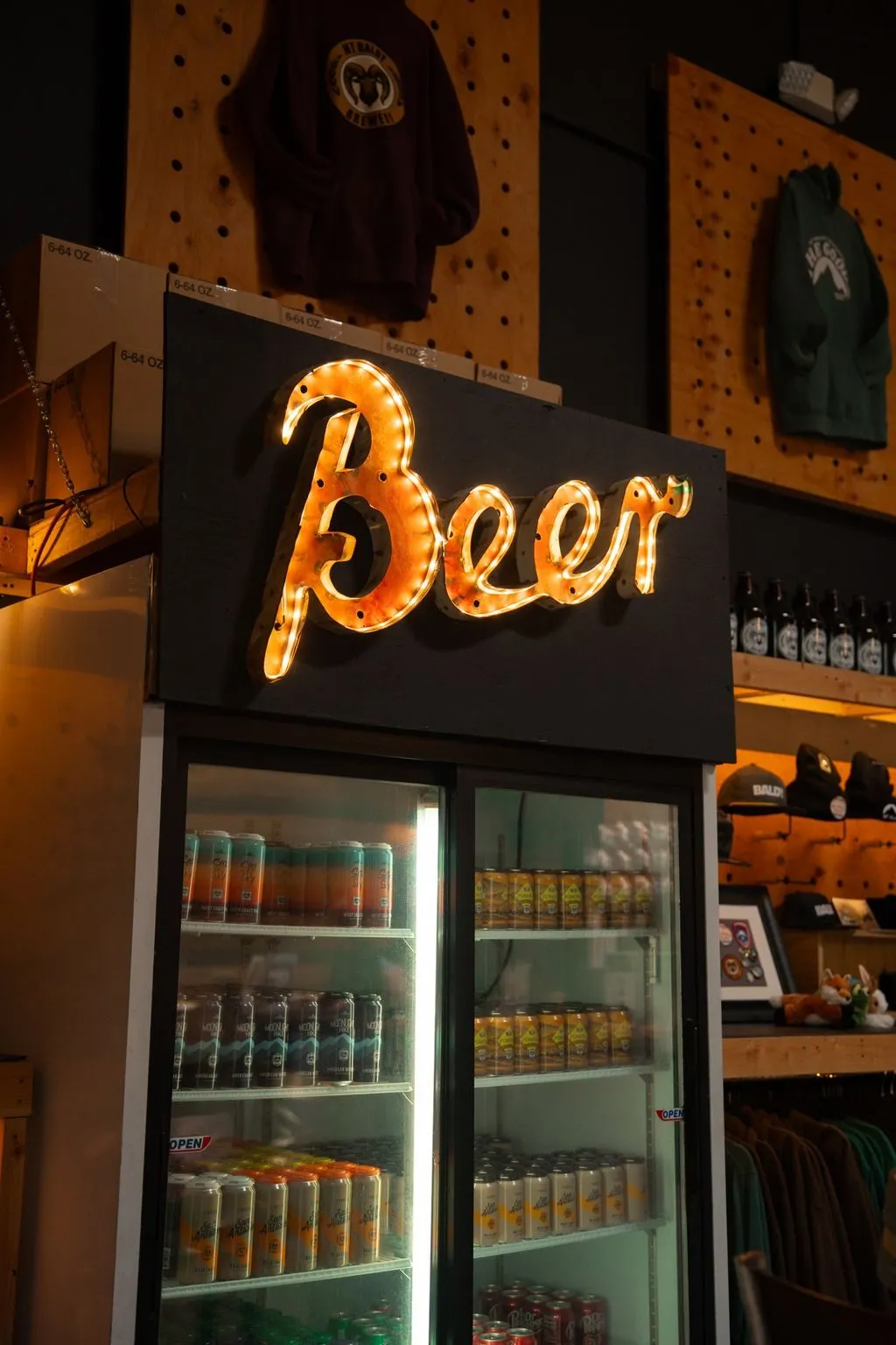 A glowing orange Beer neon sign above a fridge stocked with Mt Baldy cans
