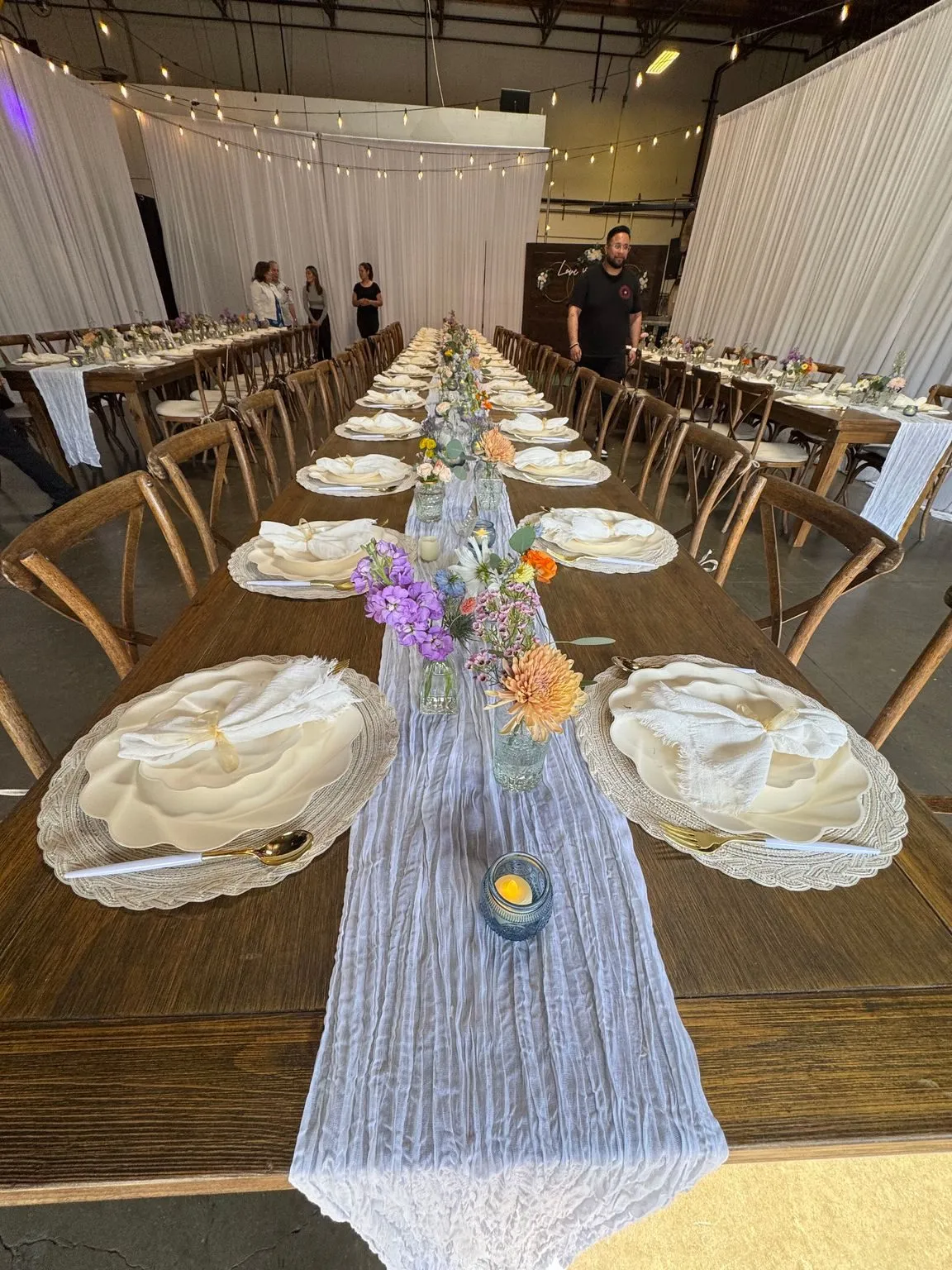 A long party table with plates, flowers and a blue runner set inside the brewery