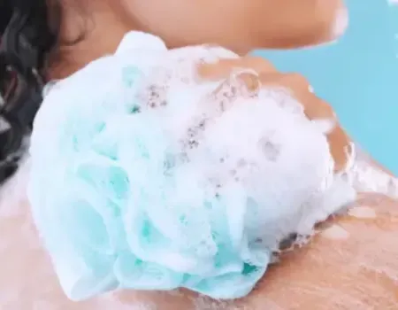 Woman scrubbing her body with a loofa and lathered soap