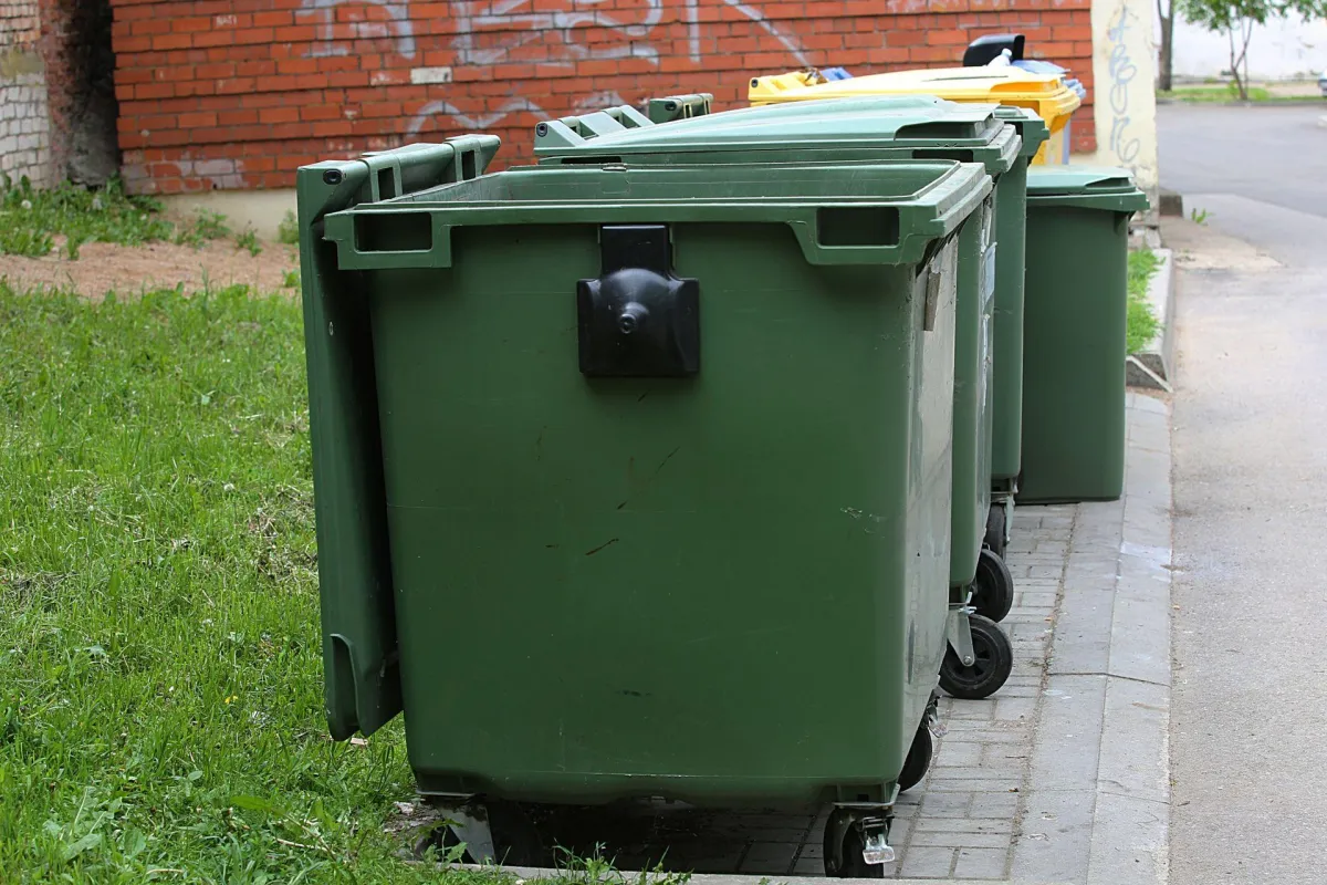 Industrial green dumpsters being cleaned with high-pressure equipment
