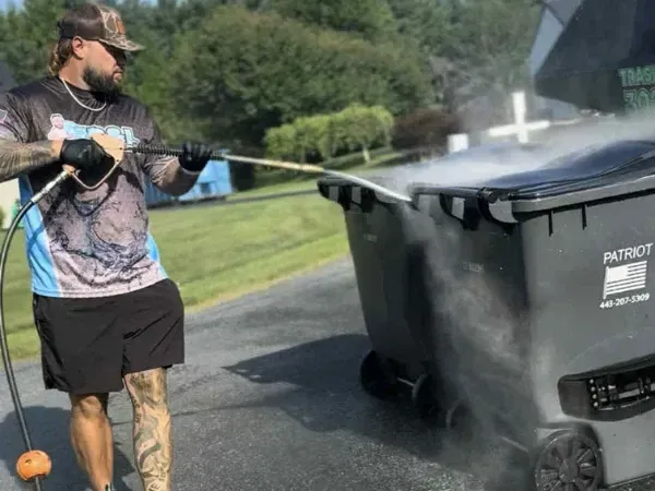 Worker using high-pressure hose to clean large outdoor trash bins