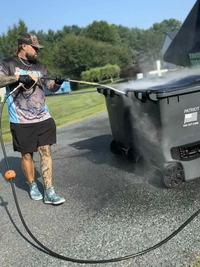 Worker using high-pressure hose to clean large outdoor trash bins