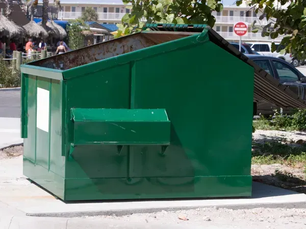 Large green commercial dumpster placed outdoors near a parking lot.