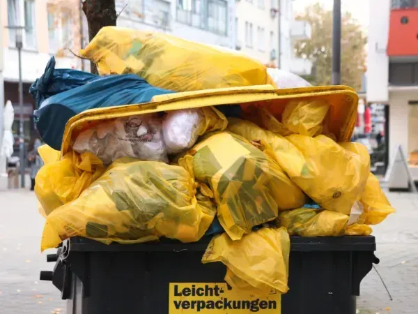 Overflowing trash bin with yellow garbage bags on a city street.
