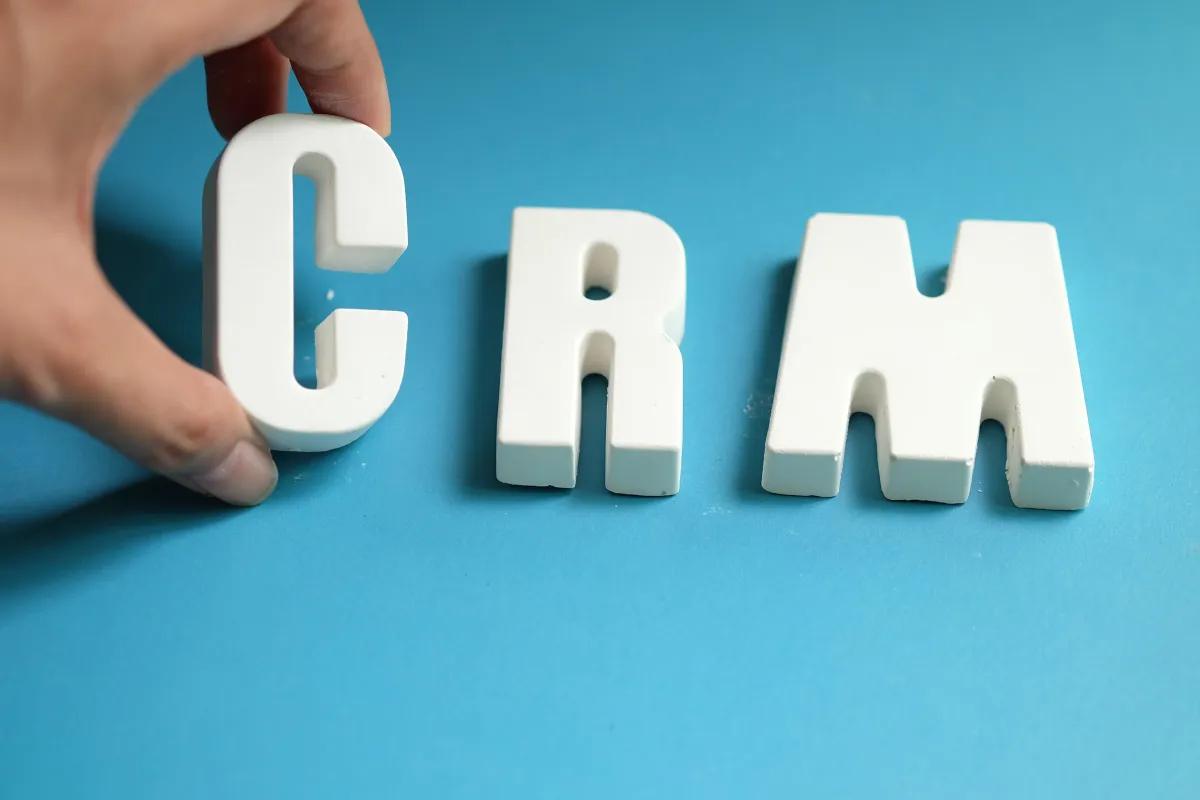 Hand arranging white letters to spell CRM, representing customer relationship management tools and strategies.