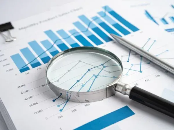 Magnifying glass resting on printed business graphs and charts showing monthly performance data.