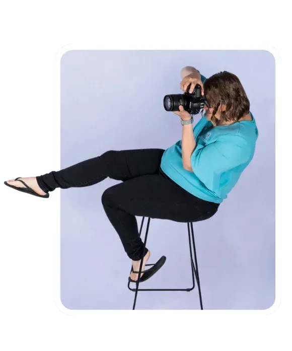 Breakout Photo of Ellie Clare, sitting on a stool taking a photo and her foot is pointing towards the content, and is breaking out of the photo frame.