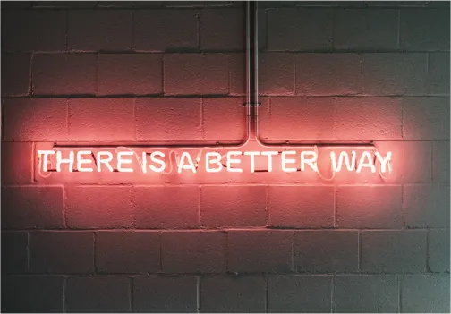 A pink neon sign on a white brick wall that reads "there is a better way"