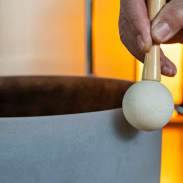 A close-up of a facilitator striking a crystal bowl during a sound meditation session.