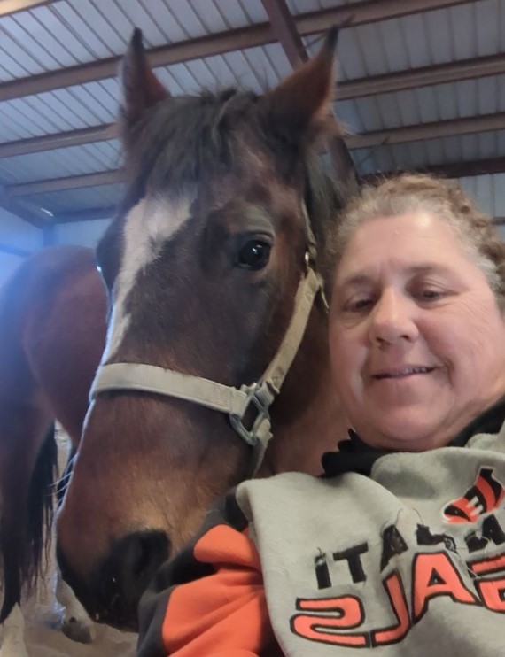 Angie interacting warmly with a horse in a pastoral setting
