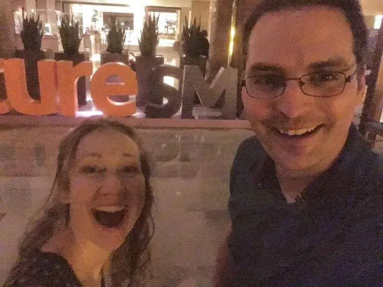 A man and woman smiling for a selfie in front of the Future MB sign, capturing a moment of joy and excitement