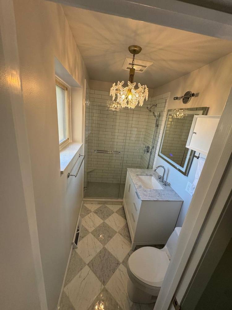 Bathroom renovation with crystal chandelier, glass shower enclosure and marble vanity