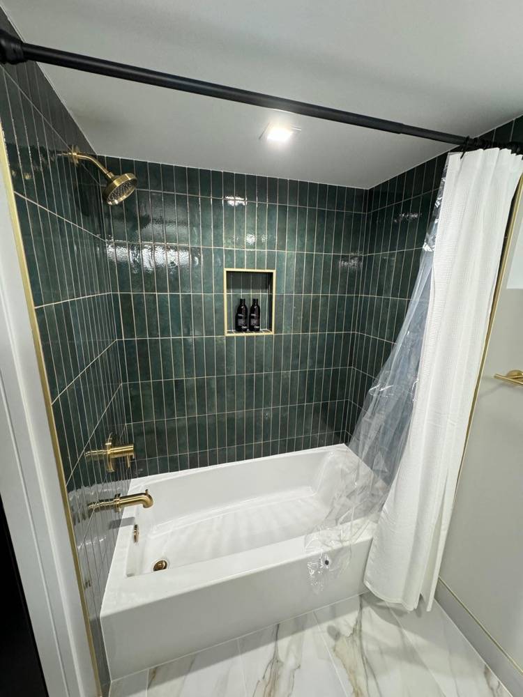 Bathroom renovation with green vertical tile surround, soaking tub and brass fixtures