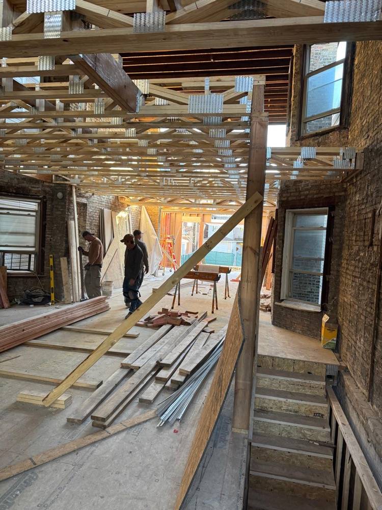Gut rehab in progress with exposed floor joists, structural bracing and crew on site