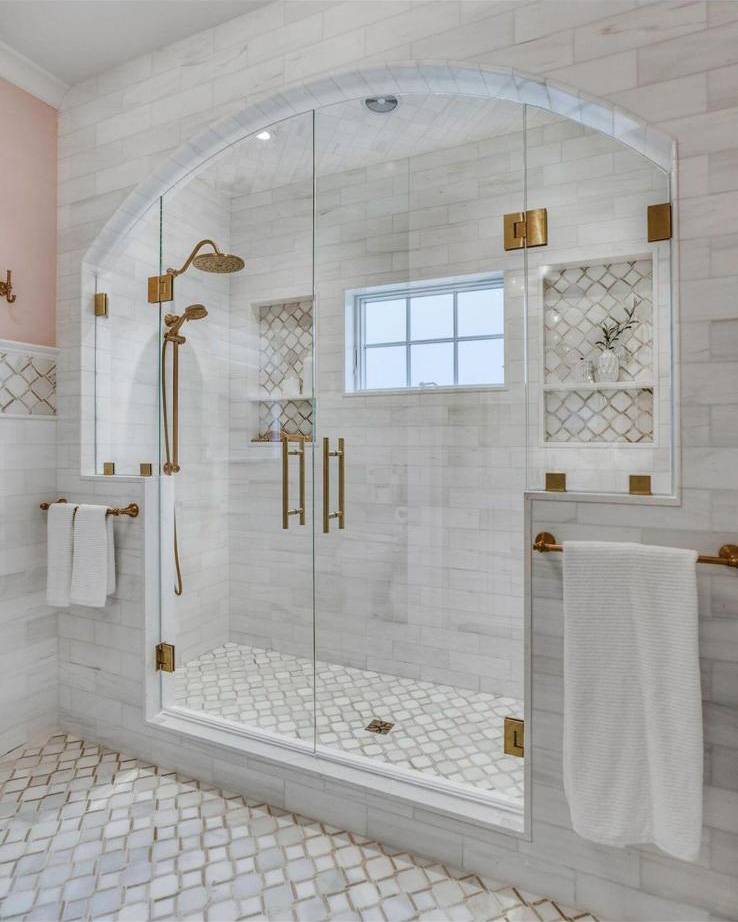 Marble walk-in shower with arched glass enclosure, brass fixtures and decorative tile niches