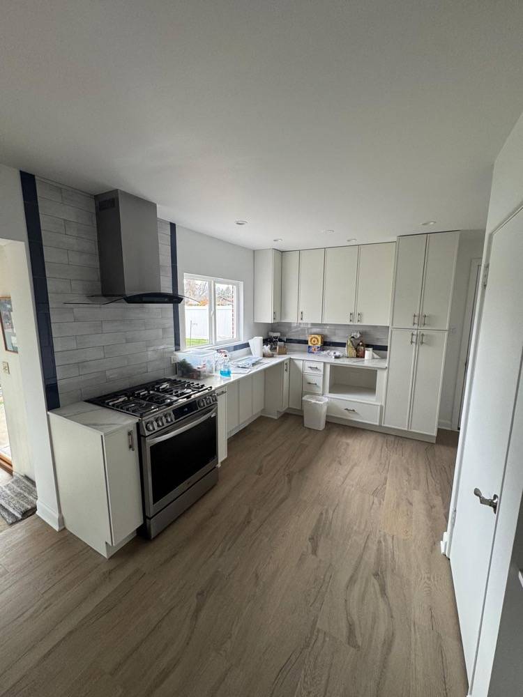 Kitchen remodel with white cabinetry, gray range hood and light wood vinyl flooring