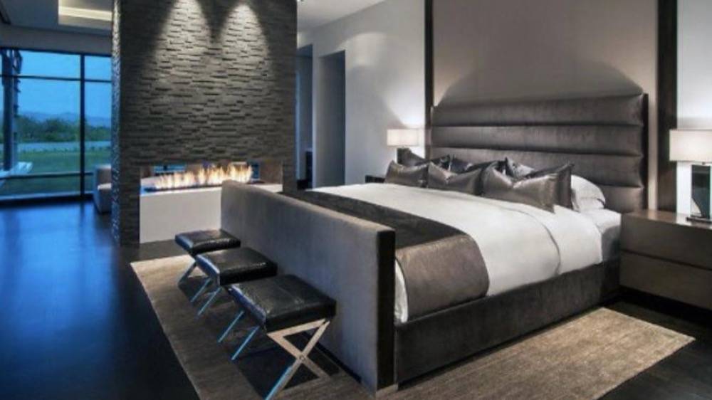 Luxury bedroom with dark stone accent wall, linear fireplace and contemporary furnishings