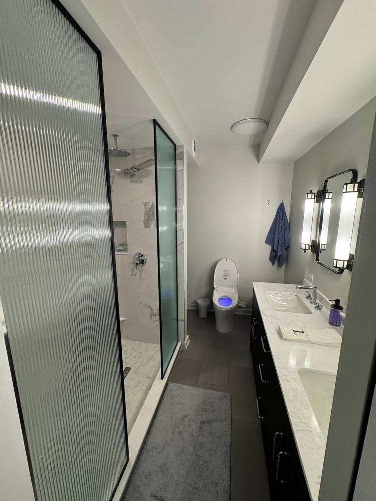 Modern bathroom with fluted glass shower enclosure, dark vanity and dual sinks