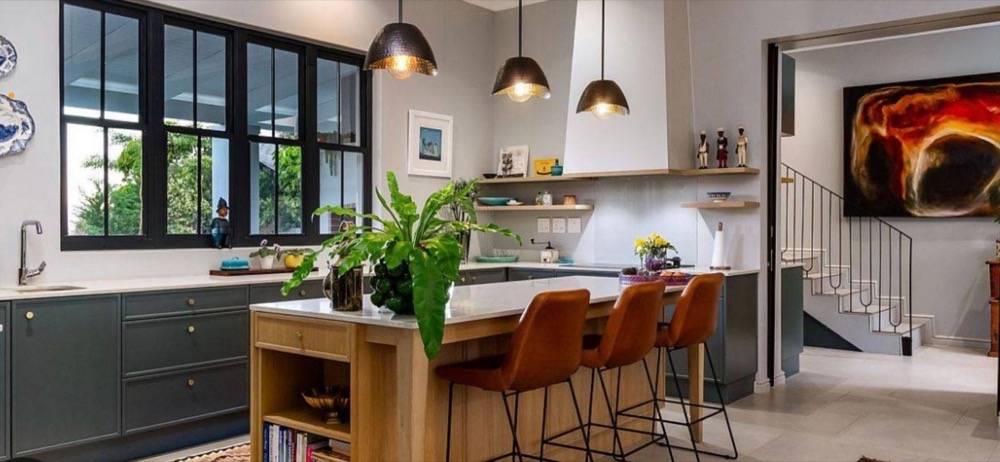 Modern open-plan kitchen with dark green cabinetry, wooden island and pendant lighting