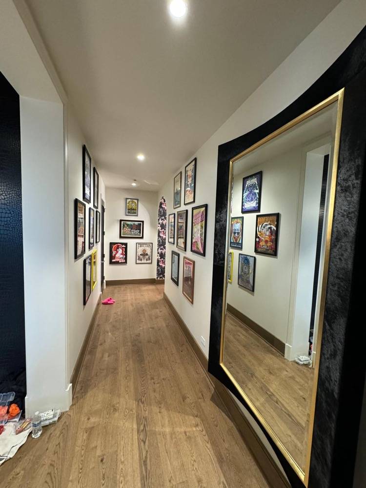 Hallway with gallery wall of framed artwork, hardwood flooring and large gold mirror