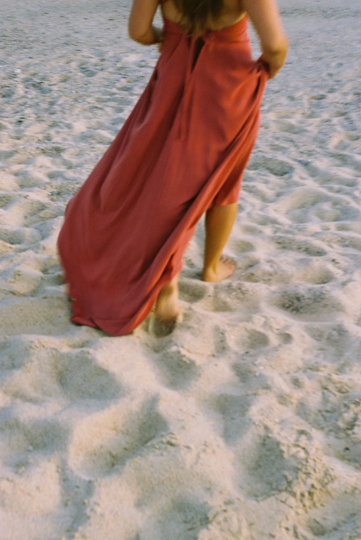 A woman in a red dress walking barefoot on the sand