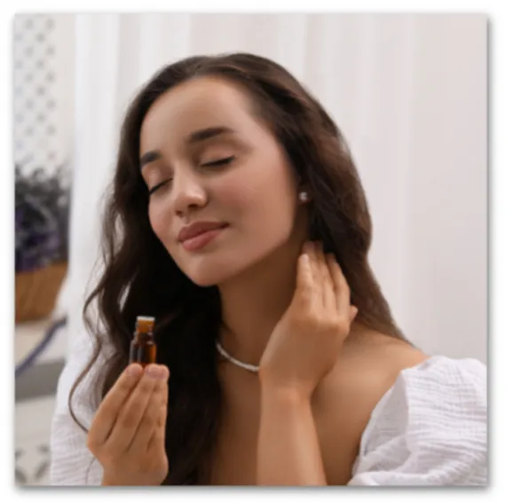 A woman with her eyes closed, holding a small amber bottle of essential oil near her nose, enjoying the scent
