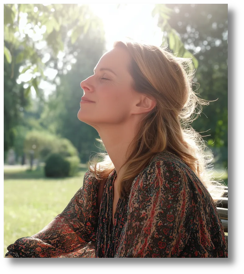 Woman in a patterned shirt sitting outdoors with her eyes closed, face tilted towards the sun, appearing peaceful.