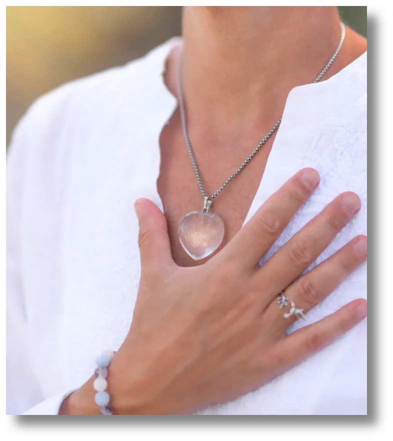 Close-up of a woman's hand resting on her chest, wearing a silver necklace with a pink stone pendant and a silver ring.