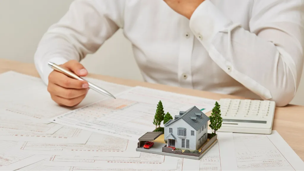 A close-up of an investor reviewing financial documents with a miniature residential property, calculator, and construction plans on the desk. The image represents property evaluation, financial analysis, and strategic decision-making before investing in or improving a real estate asset. It supports topics such as value-add multifamily investing, cash flow optimization, property improvements, investment analysis, renovation planning, operational efficiency, and value-add property improvement ideas that boost cash flow.