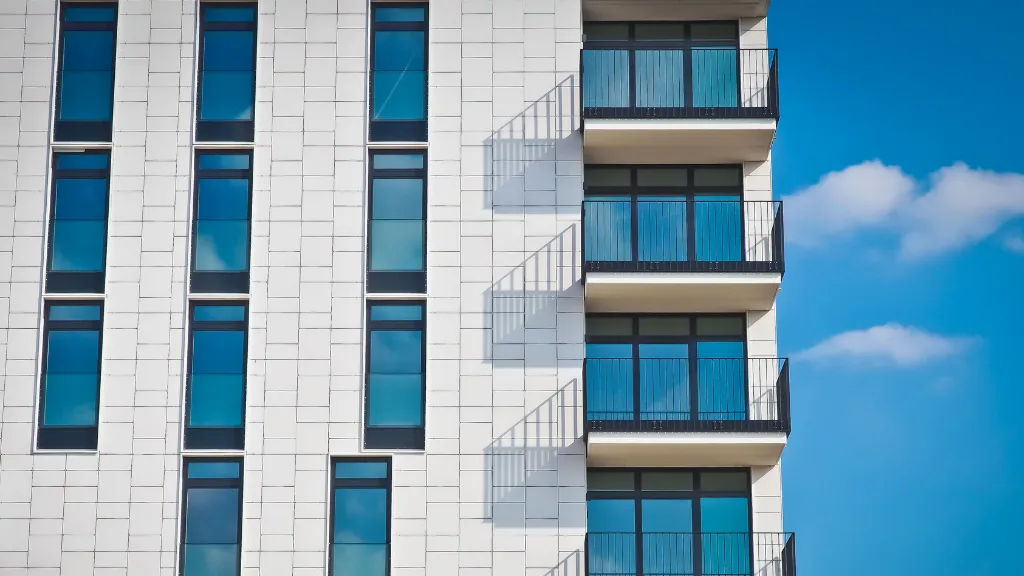 A close-up of a modern multifamily apartment building featuring clean architectural lines, large windows, and private balconies against a clear blue sky. The image represents contemporary multifamily housing, income-producing real estate, and the type of residential assets often compared with other commercial property investments. It supports topics such as multifamily investing, commercial real estate, apartment buildings, property acquisitions, investment strategy, rental properties, asset selection, and **multifamily vs. commercial real estate: which is right for you**.